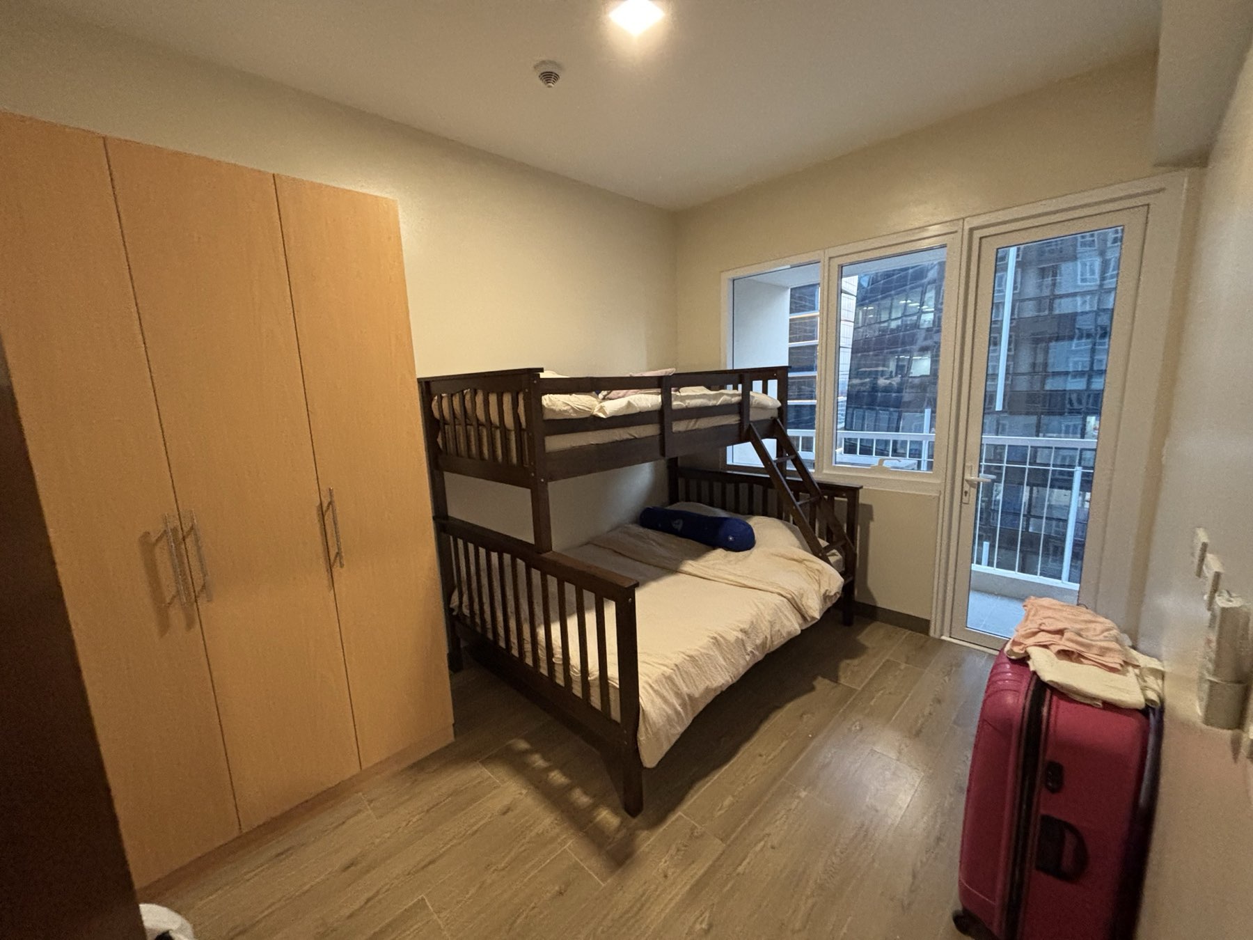 Second bedroom of the DAYON TA condo, with a bunk bed — a double below and a single above — a full-height wardrobe, and a balcony door onto the city
